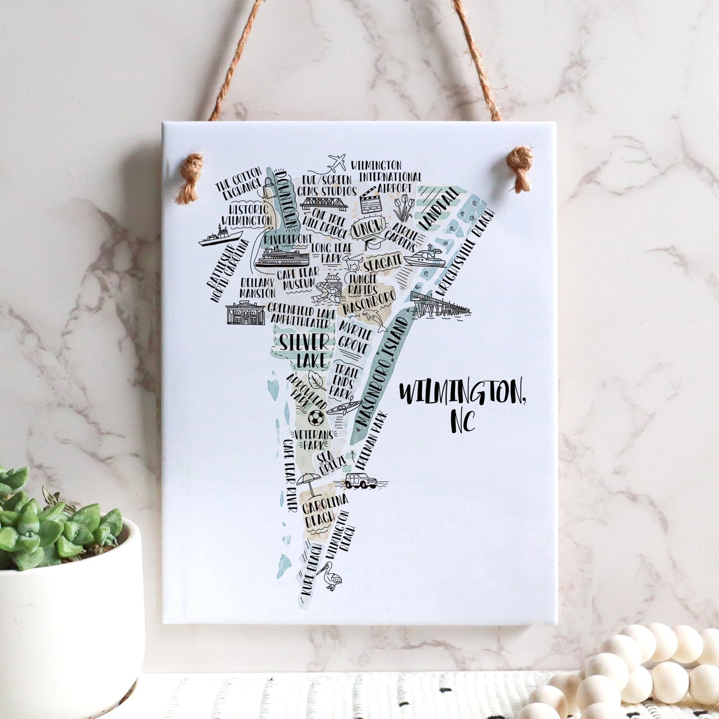 An illustrated map of Wilmington NC on a rectangle tile sign, hanging on a wall - in the color beige