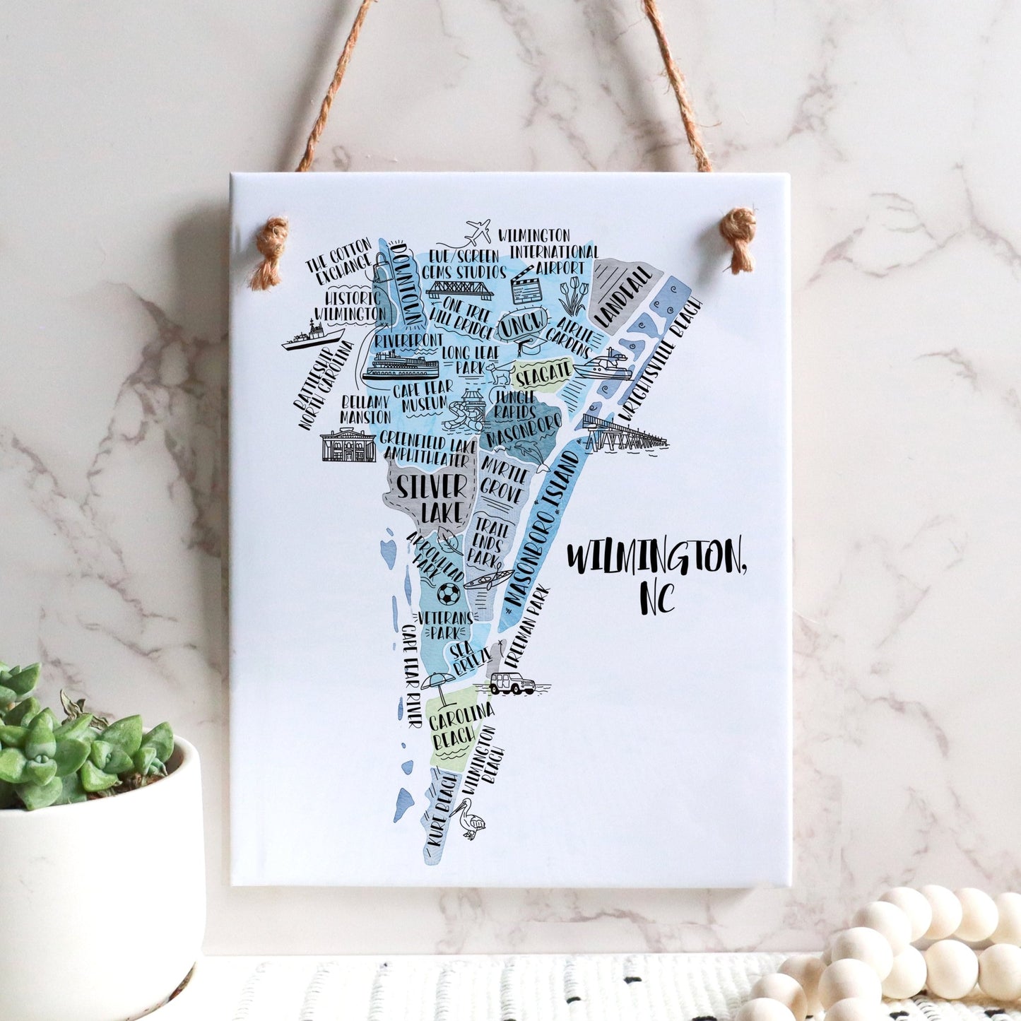 An illustrated map of Wilmington NC on a rectangle tile sign, hanging on a wall - in the color blue