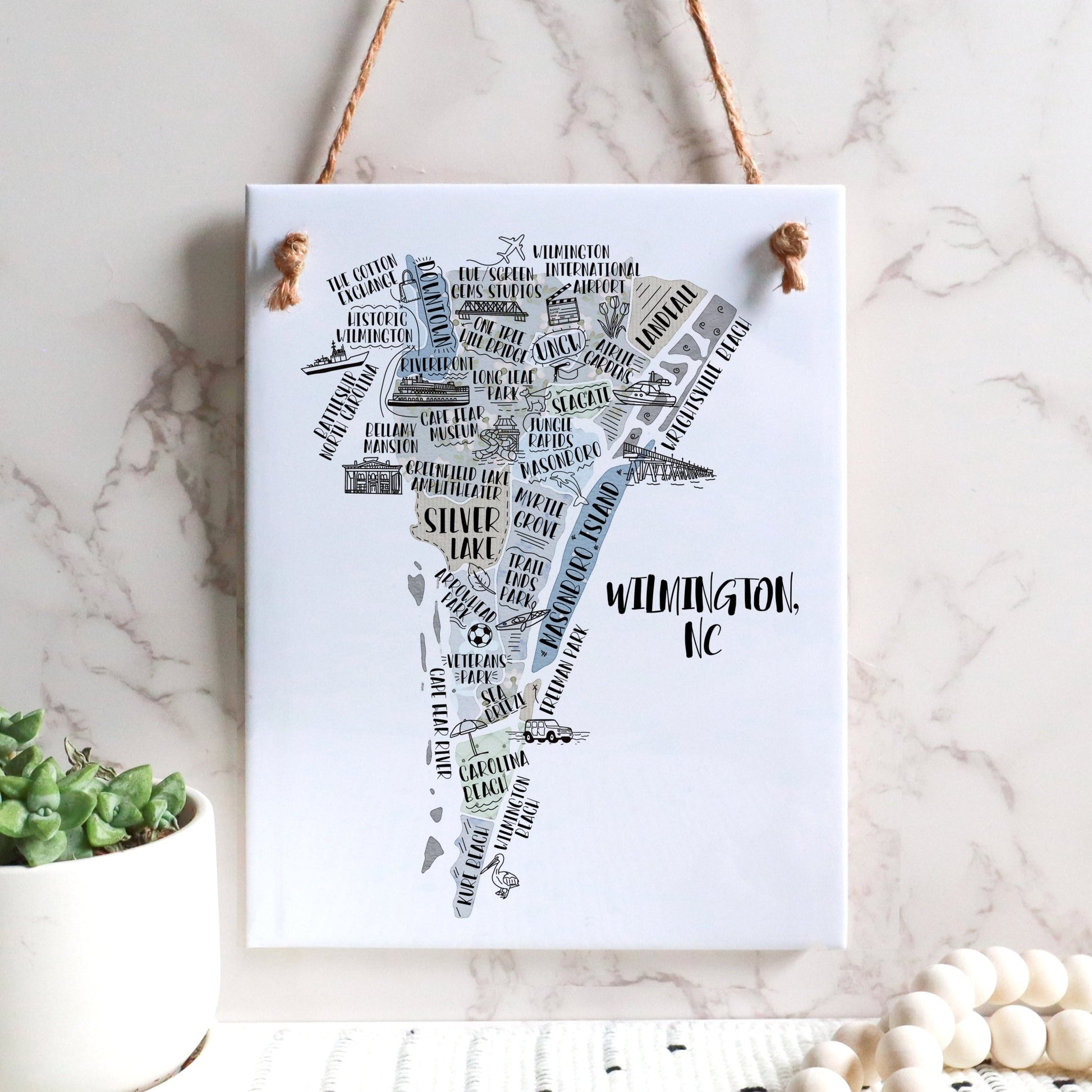 An illustrated map of Wilmington NC on a rectangle tile sign, hanging on a wall - in the color gray