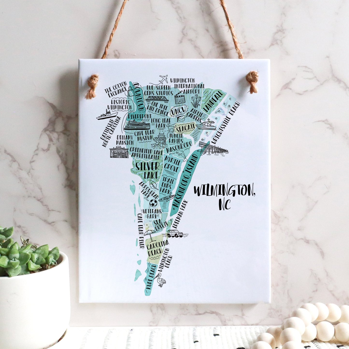 An illustrated map of Wilmington NC on a rectangle tile sign, hanging on a wall - in the color teal