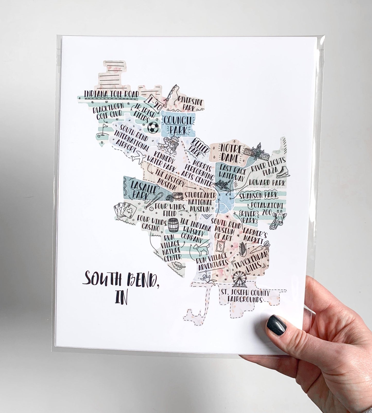 A hand holding a hand drawn city map, packaged in a clear sleeve.