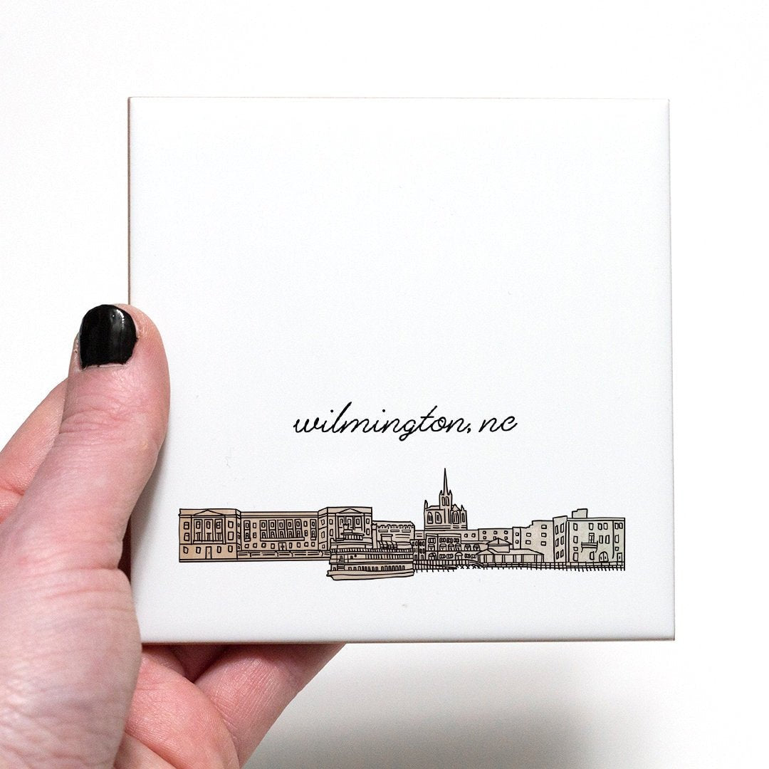 A hand holding a ceramic coaster with a city drawing of Wilmington NC - in the color beige