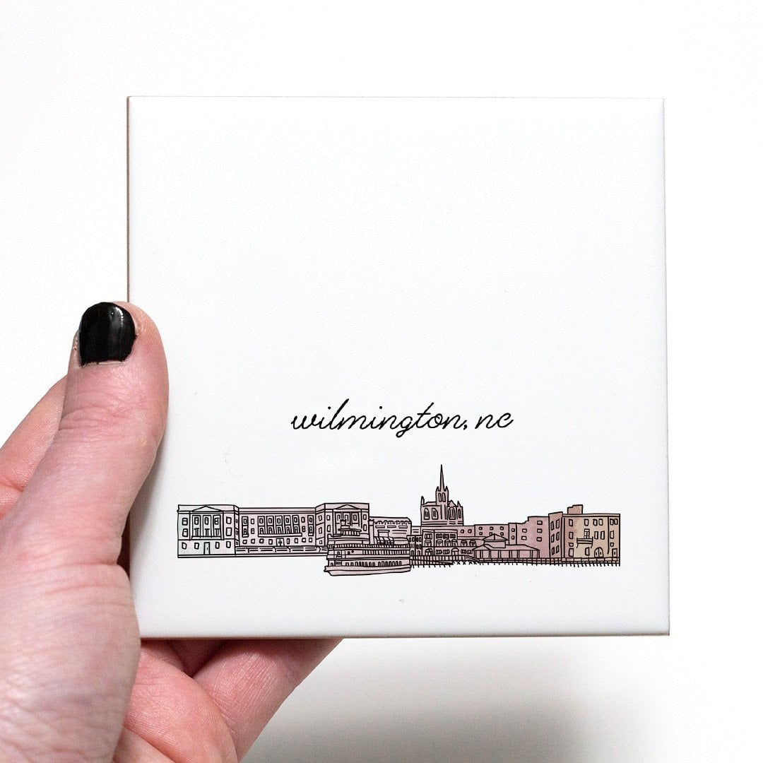 A hand holding a ceramic coaster with a city drawing of Wilmington NC - in the color blush