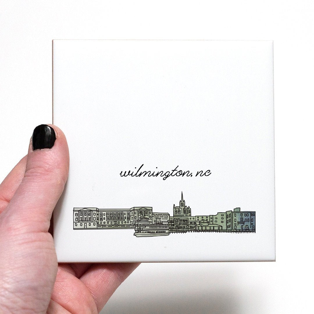 A hand holding a ceramic coaster with a city drawing of Wilmington NC - in the color green