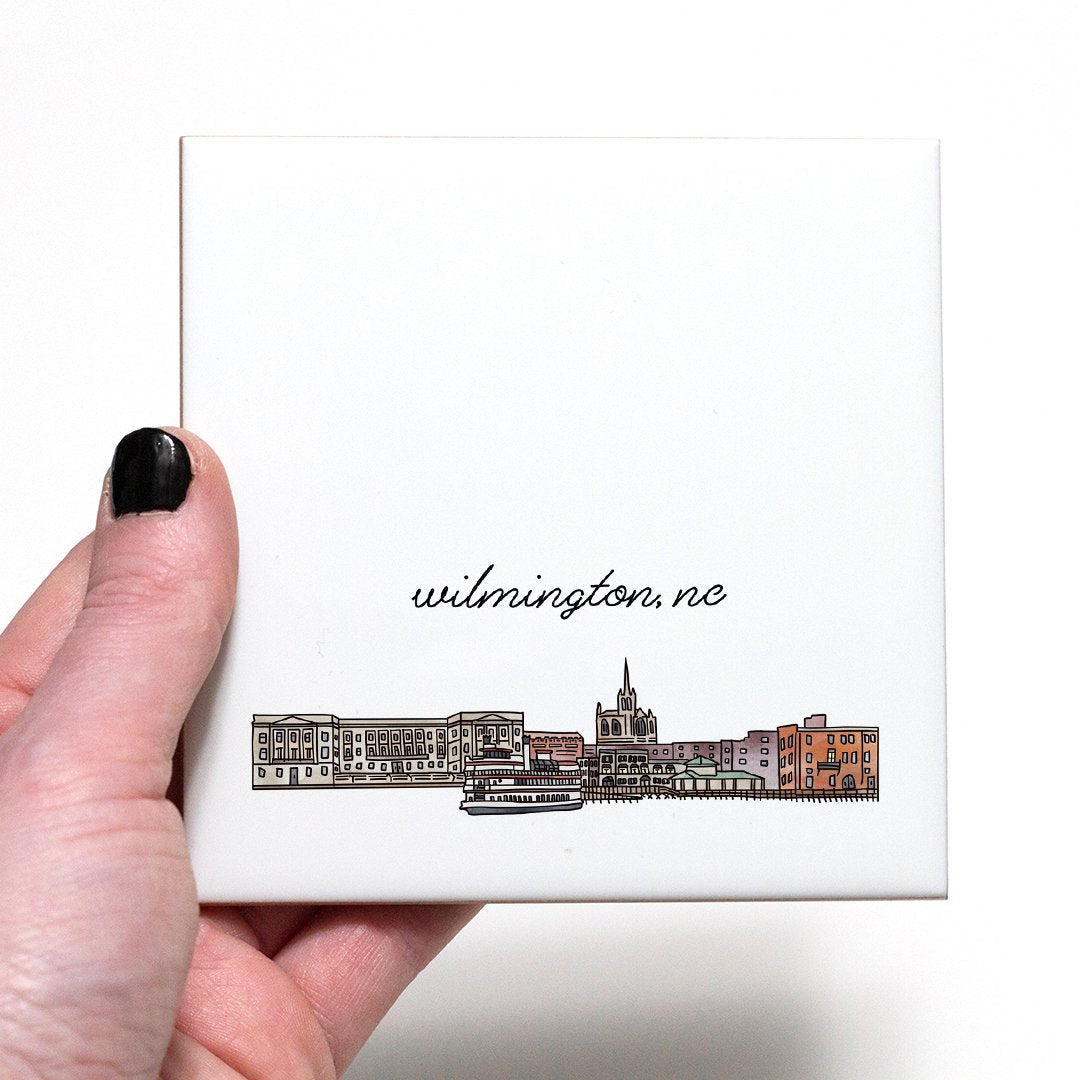 A hand holding a ceramic coaster with a city drawing of Wilmington NC - in the color natural