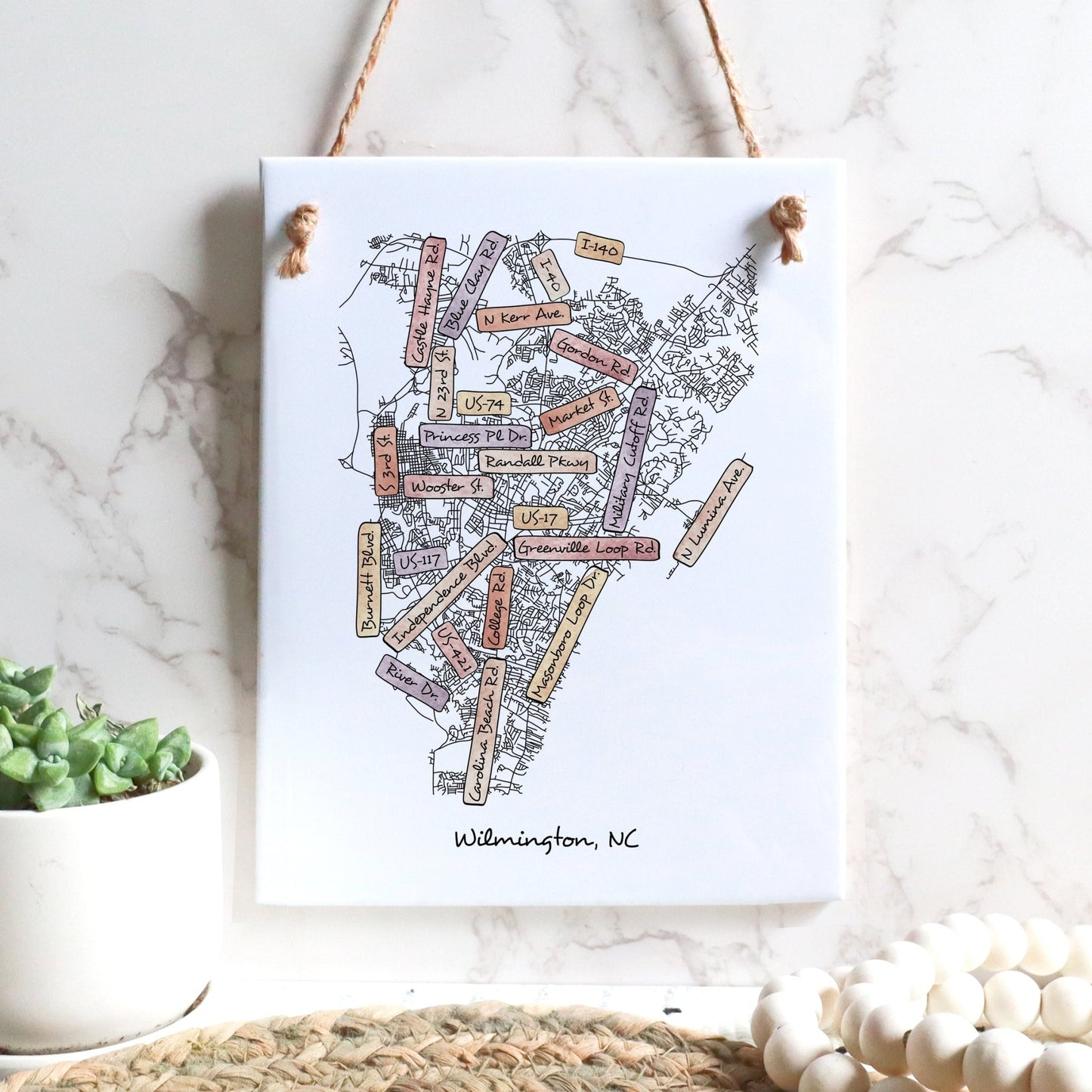 A street map drawing of Wilmington NC on a rectangle tile sign hanging on a wall - in the color sunset