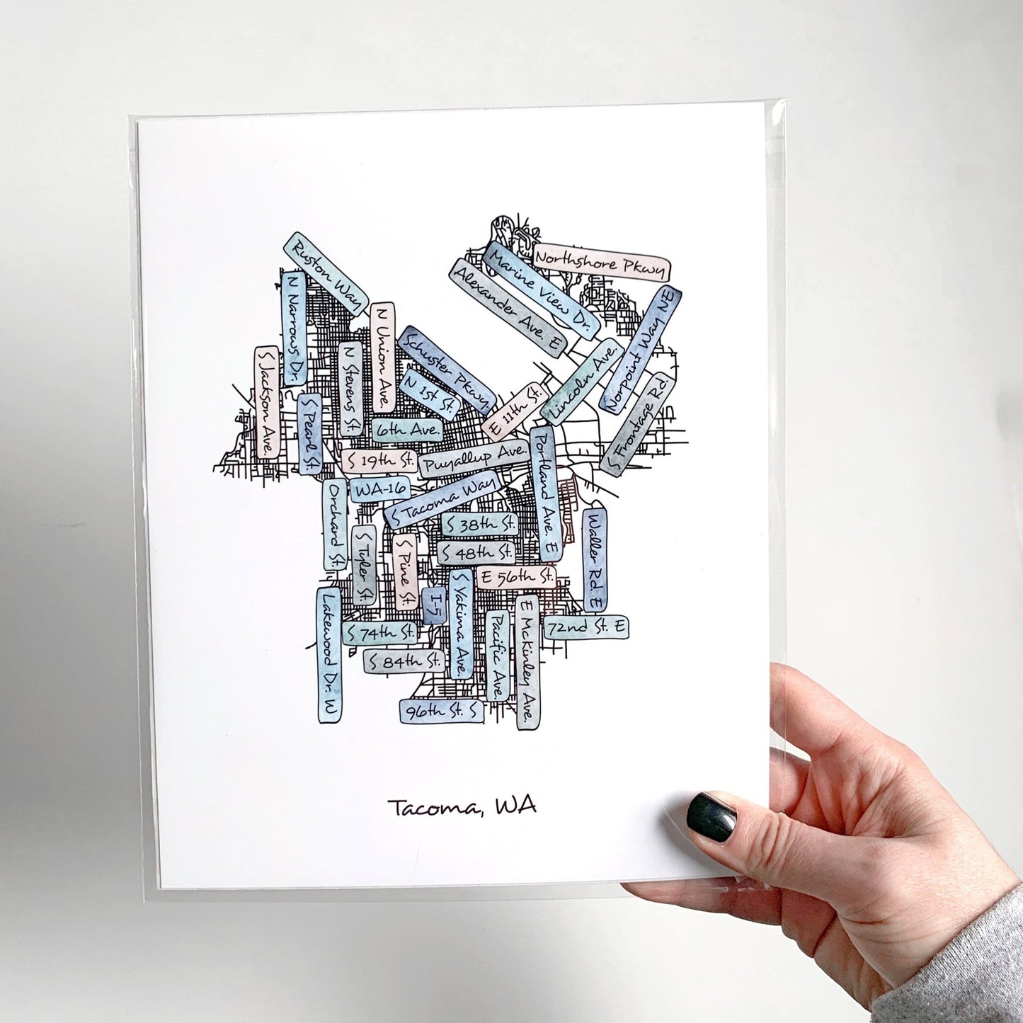 A hand holding a street map print, packaged inside a clear sleeve.